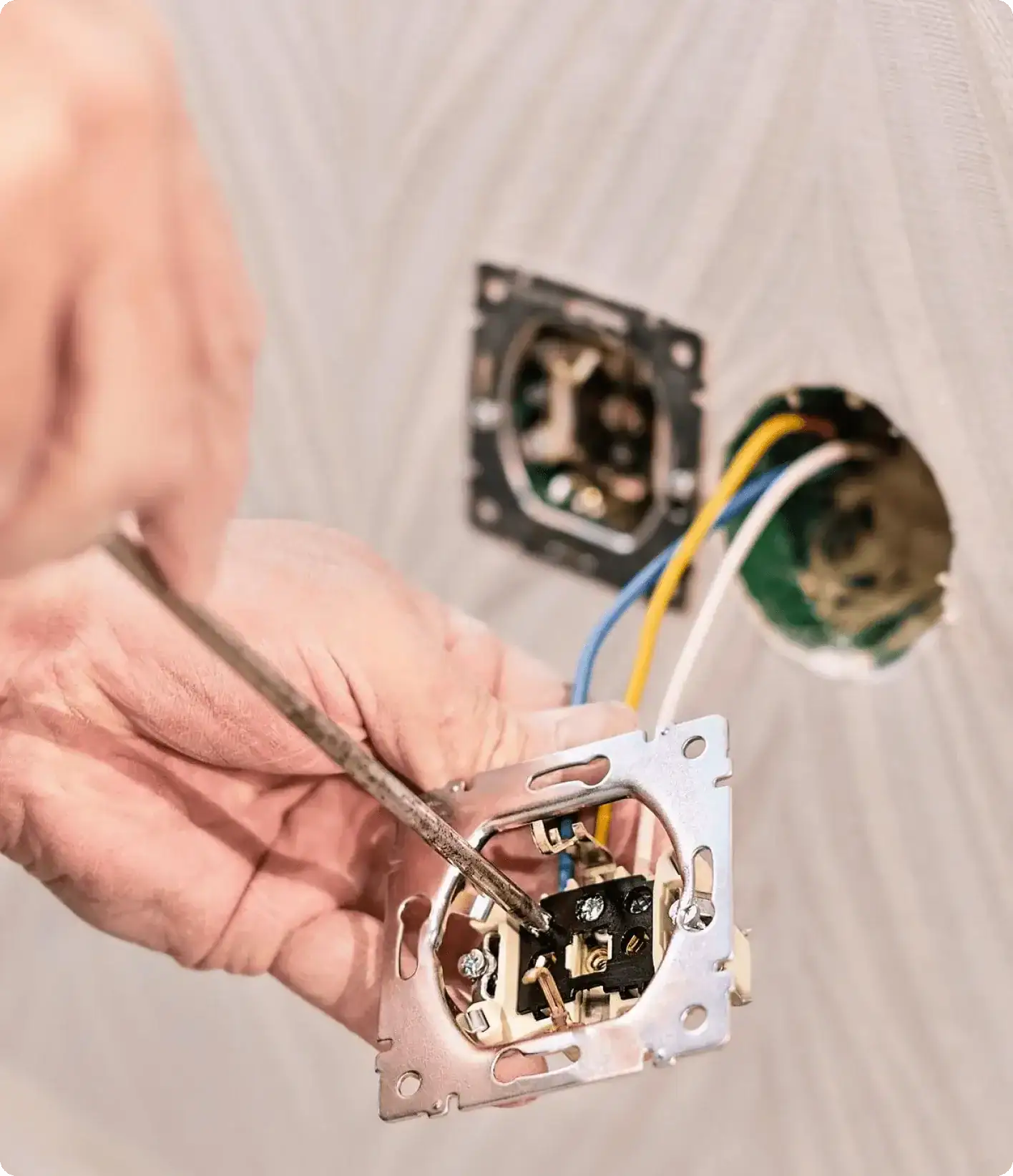 Electrician installing wall outlet with exposed wiring and electrical box during home renovation